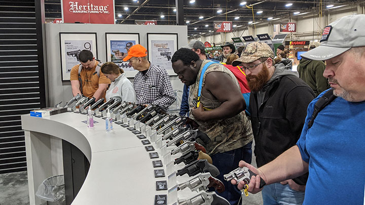Image: Several people handling firearms on display.